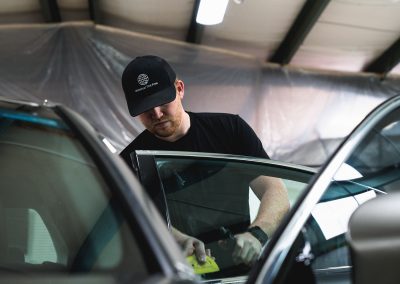 man installing car window tint in silver sedan